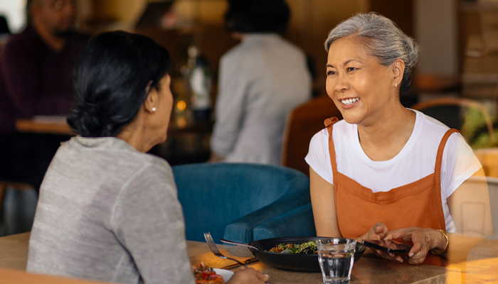 two women in a restaurant eating and talking while smiling.